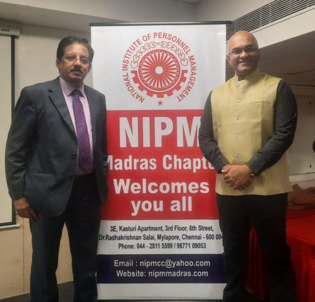 Dr. Sundararaman Chintamani with NIPM Madras Chapter welcome banner and Vinay Pushpakaran, President of Professional Speakers Association of India
