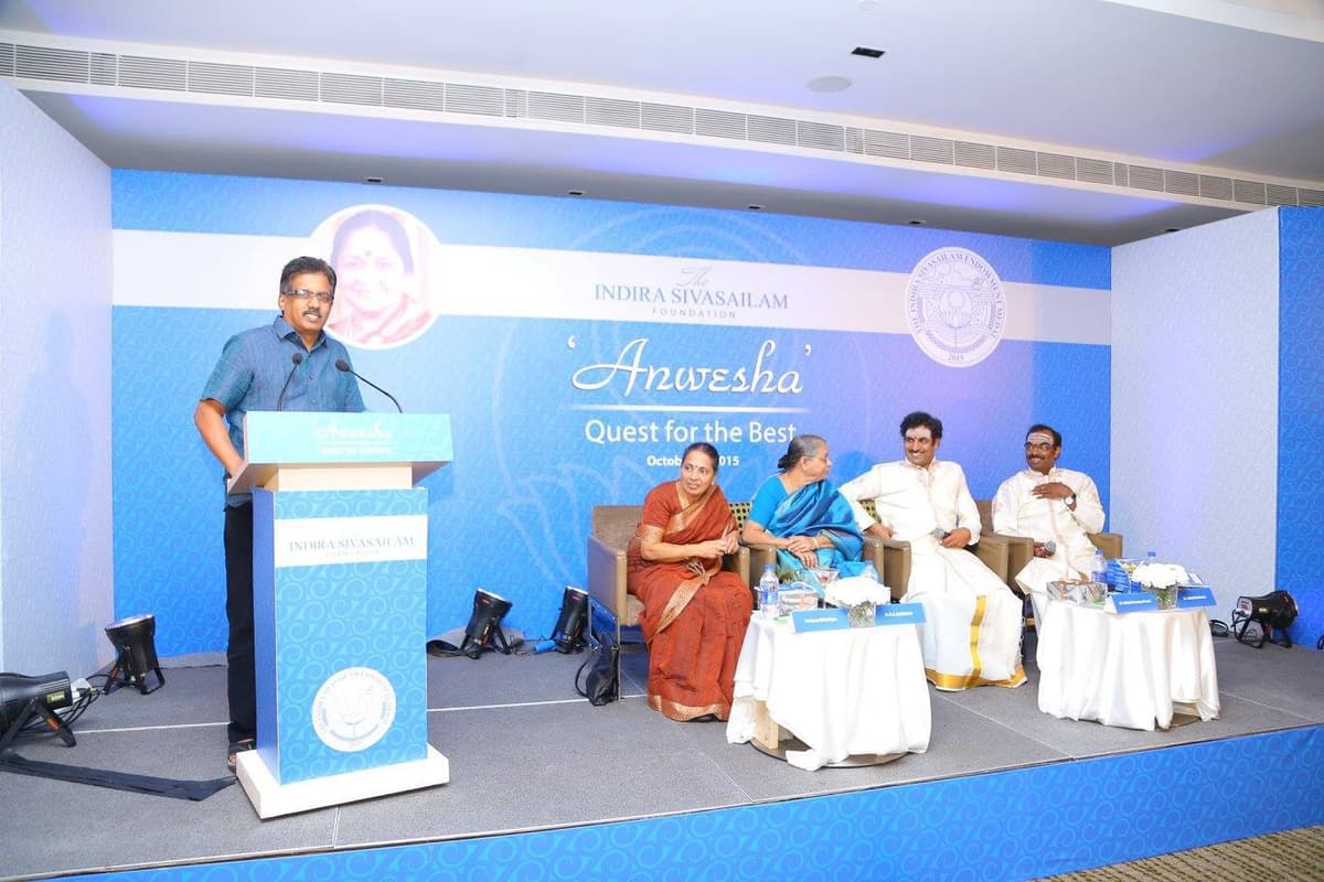 Dr. Sundararaman speaking at podium at Anwesha Quest for the Best event by Indira Sivasailam Foundation, October 2015, with Malladi Brothers on stage