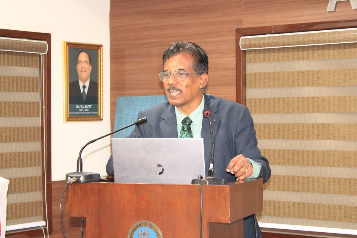 Dr. Sundararaman speaking at podium with Dr. V.L. Dutt portrait at Andhra Chamber of Commerce