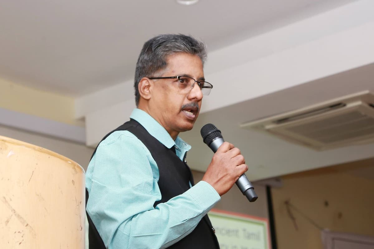Dr. Sundararaman speaking into microphone as Quiz Master at JBAS College